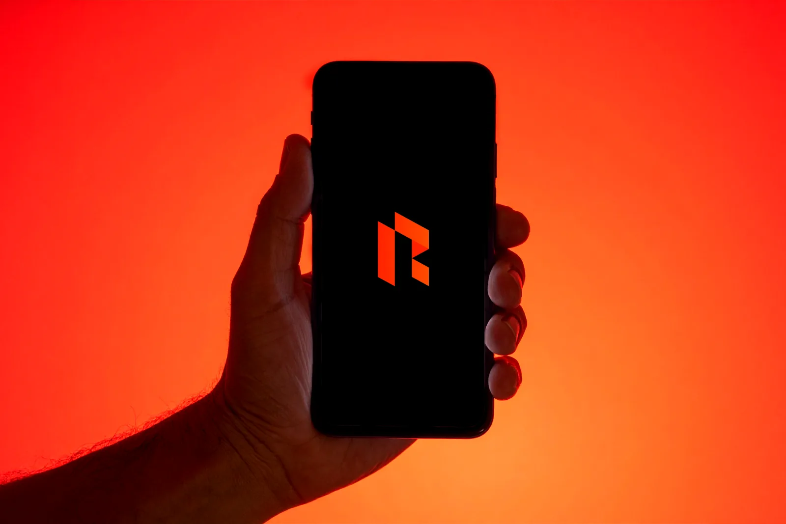 The Risknox.ai logo glowing on a smartphone screen against an orange backdrop